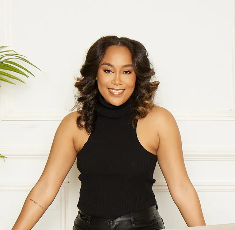 A woman wearing a black top and leather pants stands confidently, showcasing a stylish and modern outfit.